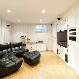 Cozy basement living area with black leather sectional, ottoman, and built-in entertainment center.