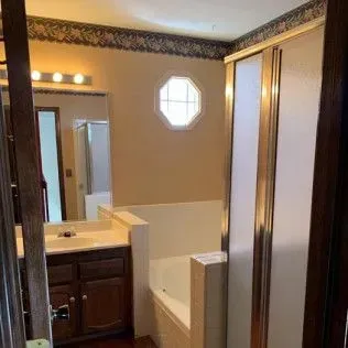 Bathroom with tub, shower, sink, and an octagonal window. Neutral-toned walls, dark cabinetry, and gold shower trim.
