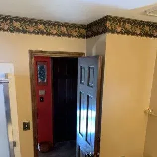 Bathroom doorway with wallpaper border, open door with red walls and dark door.