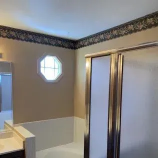 Bathroom corner with shower, octagonal window, beige walls, and floral wallpaper border.