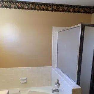 Bathroom with tan wall, floral border, white tiled wainscoting, and a glass shower.