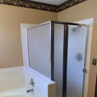Bathroom with a shower stall featuring frosted glass doors, beige walls, and a floral border.