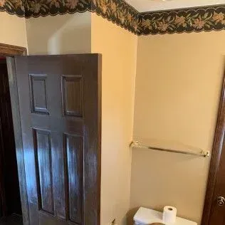 Brown door and beige walls with decorative wallpaper border, bathroom setting.