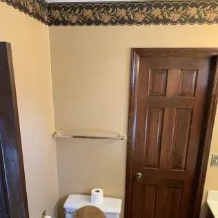 Bathroom interior with tan walls, brown door, floral wallpaper border, and toilet.