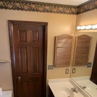 Bathroom with a wooden door, vanity, and a mirror. Wallpaper border.