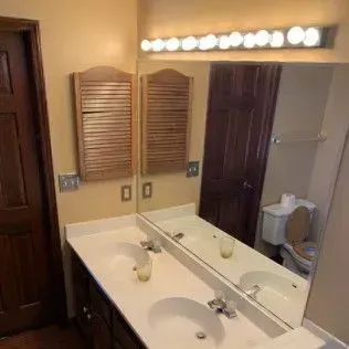 Bathroom with a double vanity, mirror, wooden cabinets, and a toilet.