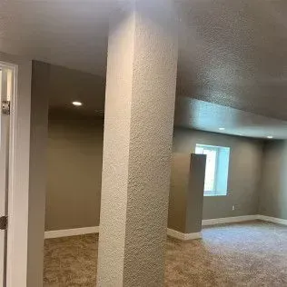 Interior of a room with a textured column, beige walls, carpet, and a window.