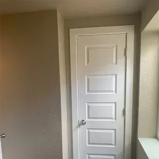 White door with four rectangular panels in a neutral-colored hallway.