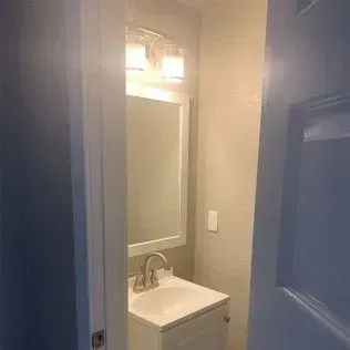 Bathroom interior with sink, mirror, and overhead lighting seen from a doorway.
