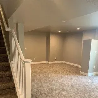 Staircase leading to a finished basement with beige walls, carpet, and recessed lighting.
