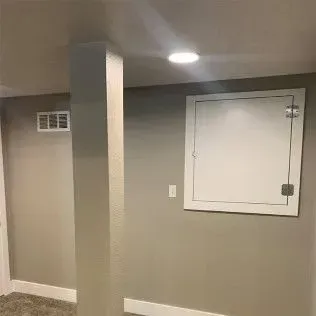 A basement interior featuring a white access panel, a support pillar, and a ventilation grate.