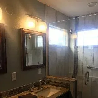 Bathroom with vanity, mirror, shower, and window. Beige and brown tones.