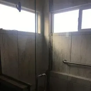 Bathroom shower with glass door and handrail. Light colored tiled walls.