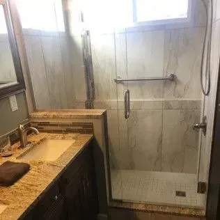 Bathroom with granite countertop, dark cabinet, and tiled shower with grab bar.