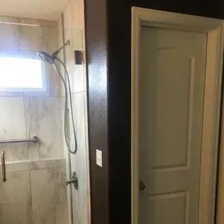 Shower with handheld sprayer and white door in a bathroom. Dark wall separating the two.