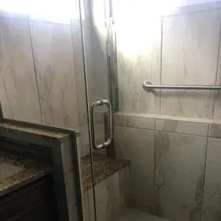 Shower stall with glass door and grab bar. Beige tiled walls.