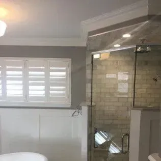 Bathroom with white shutters, a glass shower, and gray walls.