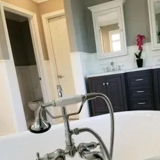 Bathroom with bathtub and faucet in foreground, vanity with mirror, and toilet.