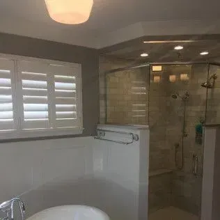 Bathroom interior with a shower, bathtub, and window with shutters.