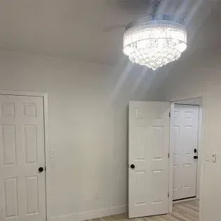 Interior of a room with white walls, three doors, and a crystal chandelier.