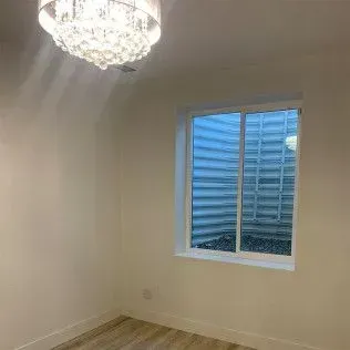 Empty room with a window and a chandelier. The window faces an exterior well. The walls are white.