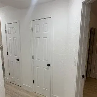 White hallway with two closed doors and a doorway.