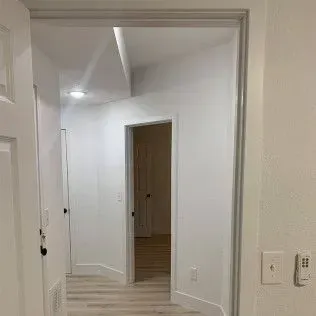 Hallway with white walls, doors, and a light-colored wood floor.