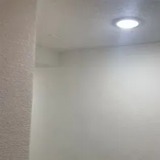 Empty, white-walled room with a recessed ceiling light. Textured wall on left.