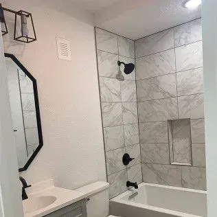 Bathroom with white walls, black fixtures, tiled shower, and a bathtub.