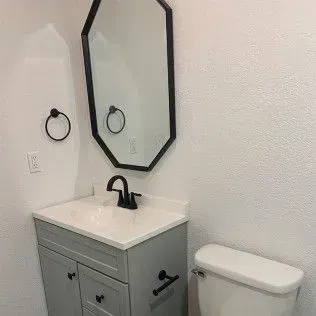 Bathroom with a gray vanity, black faucet and mirror, toilet, and towel ring.