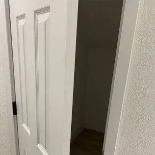 White door slightly ajar, revealing a dark closet interior with light-colored flooring.