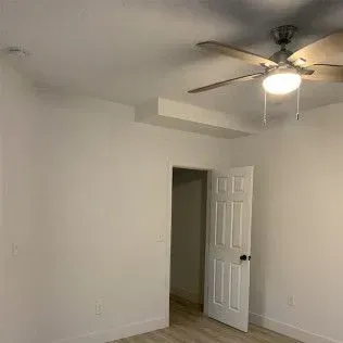 A white room with a ceiling fan, door, and a partially open doorway leading to a dark hallway.