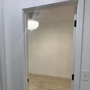 White doorway opening into a room with white walls, wood-look floor, and a chandelier.