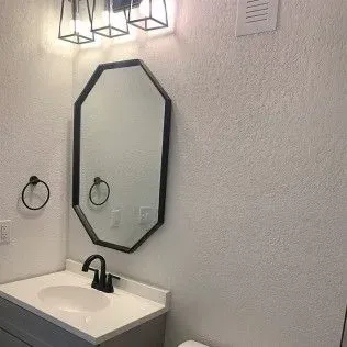 Bathroom with a black-framed mirror, sink, and light fixture. The walls are textured and white.