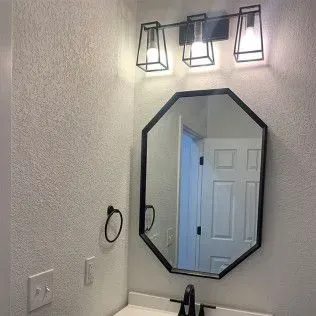 Bathroom with black-framed octagon mirror, black light fixture, and black faucet. Gray walls, white door.