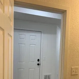 White doorframe leading to an interior door, white walls, and a light-colored wall on the right.