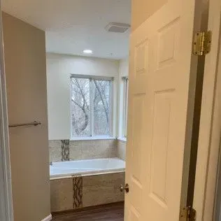 Bathroom entrance with open door, view of bathtub, window, and wall.