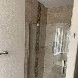 A bathroom with a tiled shower. Clear glass door and a small window are visible inside.