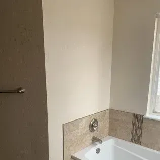 Bathroom corner with off-white walls, beige tile, and a white tub with faucet.