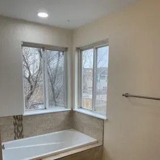 Bathroom with bathtub, windows, and neutral-colored walls and tile. Towel rack on the wall.