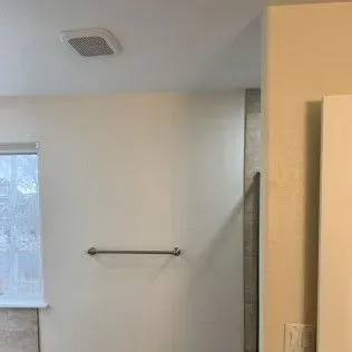 Bathroom interior with a window, towel bar, and ceiling vent. White walls.