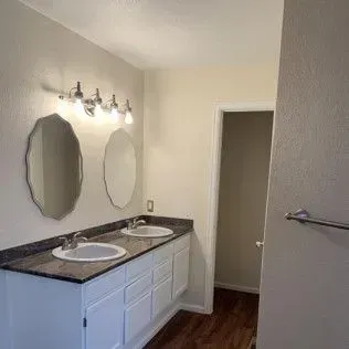 Bathroom with double sinks, mirrors, and a door to another room.