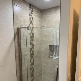 Shower with beige tiled walls, a glass door, and decorative vertical tile strip.