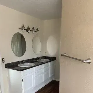 Bathroom with white vanity, black countertop, two sinks, and oval mirrors.