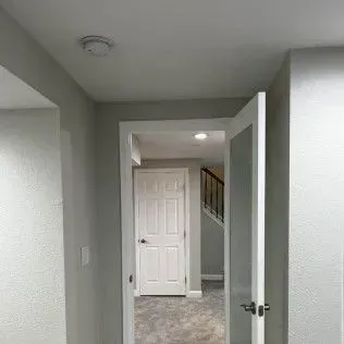 Hallway with open door revealing a staircase and another closed door. Light gray walls, white trim.