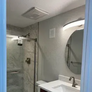 Bathroom with shower, mirror, sink, ventilation fan, and light fixtures.