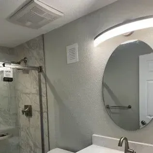 Bathroom with shower, mirror, sink, and overhead light. Gray walls and tile.