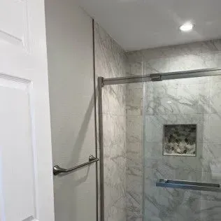 Bathroom with gray marble tiles, glass shower door, and recessed shelf.