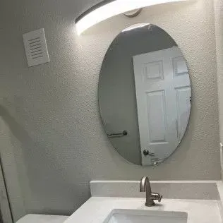 Bathroom with oval mirror, white sink, faucet, and overhead light. White door reflection.