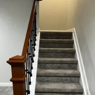 Staircase with carpeted steps, a dark wooden banister with black spindles, and light gray walls.